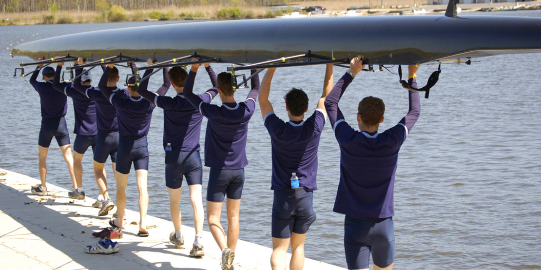 photo of crew team on dock carrying boat together towards water